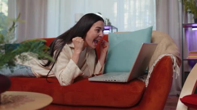在笔记本电脑上工作的喜出望外的年轻女子庆祝成功在彩票中赢钱获得在线好消息