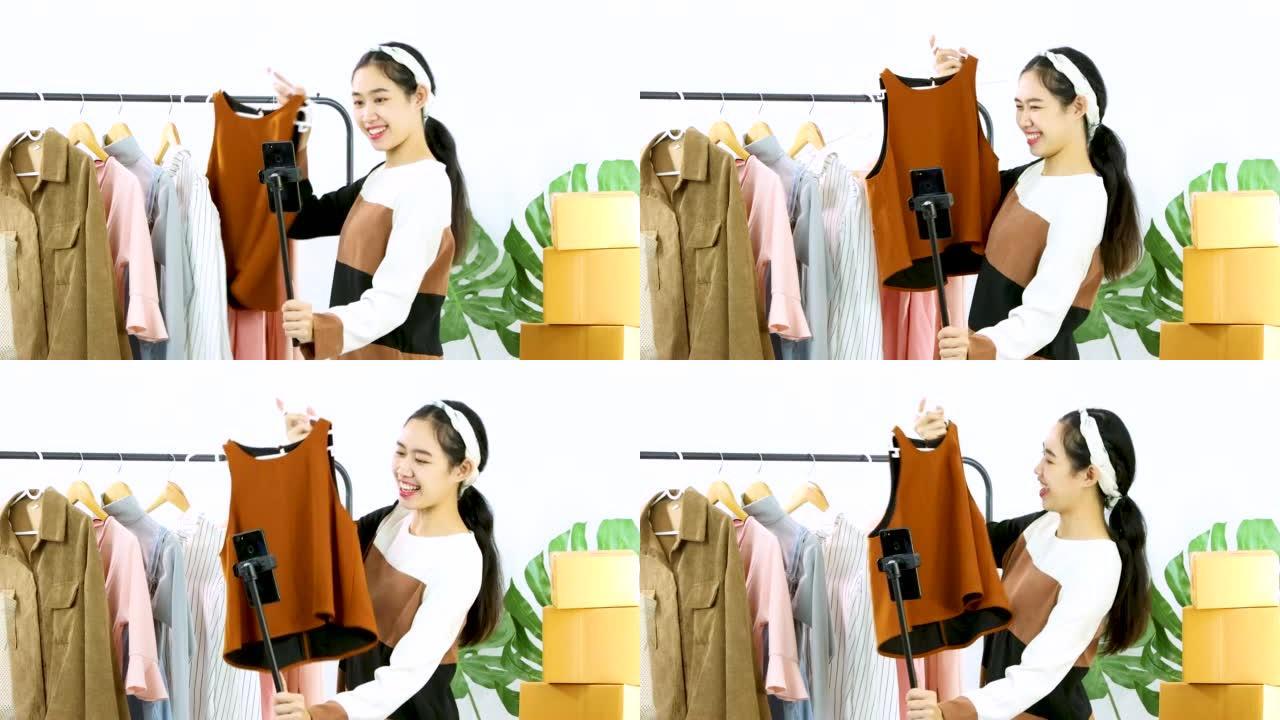 年轻的亚洲女性时尚视频记录器向智能手机摄像头展示衣服记录视频直播在线商店在家销售。直播视频4K。