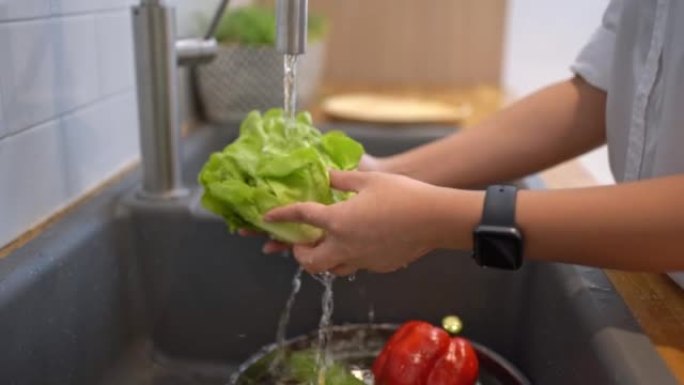 一位亚洲妇女的手在厨房里洗绿色蔬菜。健康的生活方式