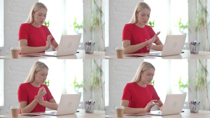 年轻的金发女人在办公室使用笔记本电脑时手腕疼痛