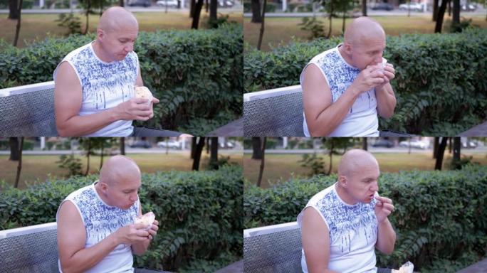 饥饿的男性在长凳上休息，在街上的公园里吃沙瓦玛面包