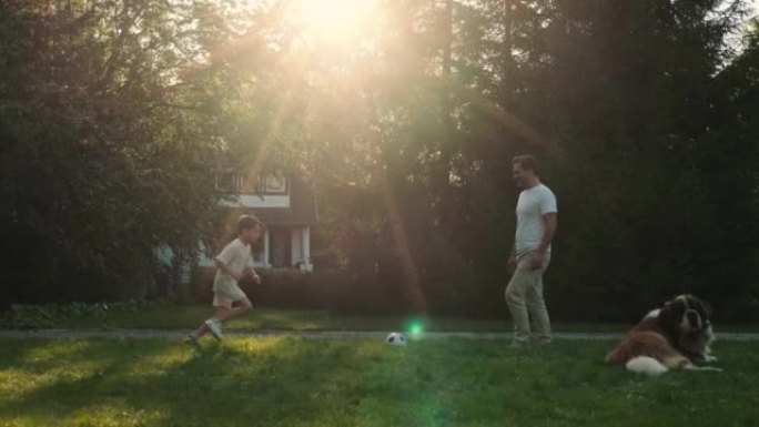 日落时，爸爸和儿子在草坪上踢足球。