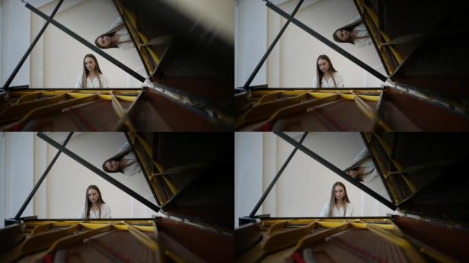 特写镜头从三角钢琴打开的盖子到才华横溢的年轻女钢琴家穿着优雅的休闲服在白色背景的乐器上演奏。