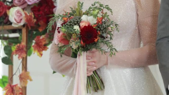 婚礼庆典上新娘手中的美丽婚礼花束。节日女装背景下红色、粉色、白色柔和颜色和绿色花朵的特写视图