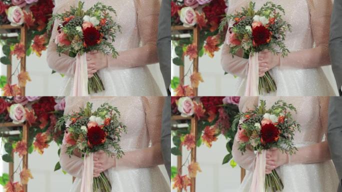 婚礼庆典上新娘手中的美丽婚礼花束。节日女装背景下红色、粉色、白色柔和颜色和绿色花朵的特写视图