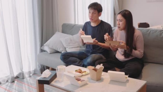 周末，一对亚洲夫妇家庭在客厅的电视前享受外卖食物