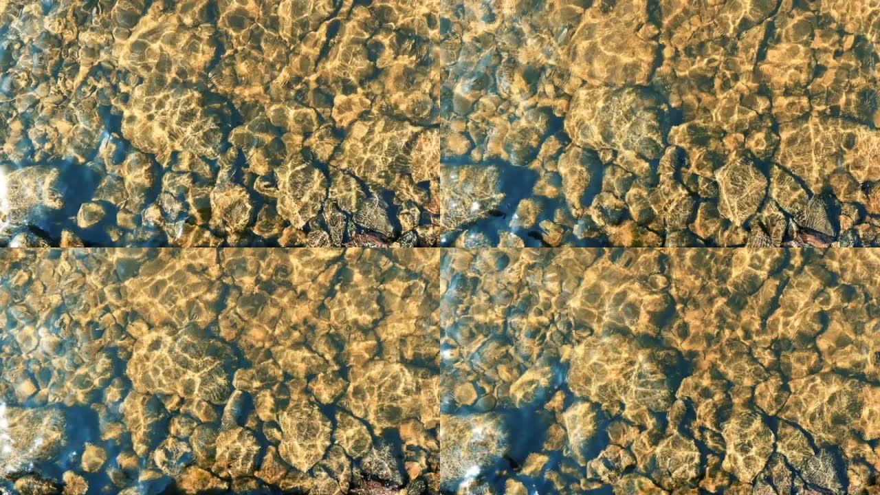 水下的彩色石头。泉水流经不同的石头。顶视图。五彩石头上的水反射