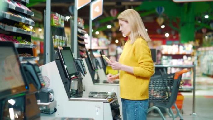 在超市使用自助收银台结账的女性买家。客户扫描在杂货店自助收银机上生产物品