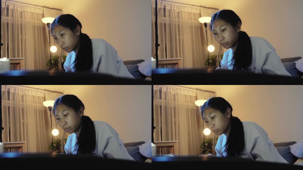 亚洲女孩在家里的夜晚通过沙发上的移动应用学习弹奏键盘乐器，生活方式理念。