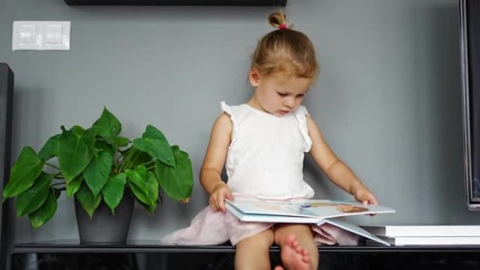 可爱的蹒跚学步的小女孩在家看书。幼儿园的幸福儿童读物享受自己的学习教育。教育理念