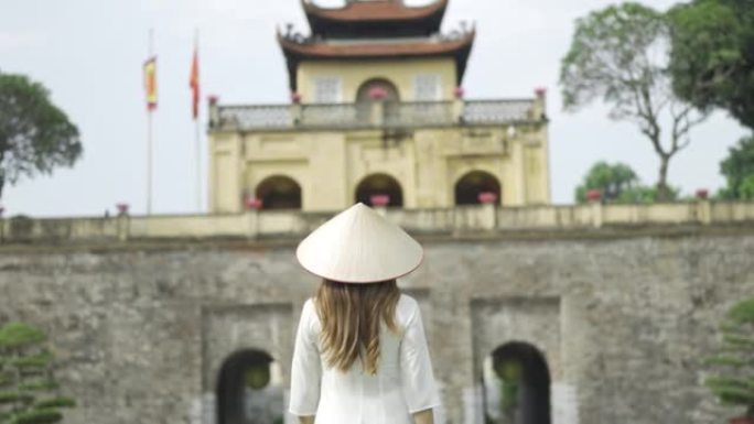 越南女子穿着传统服饰，戴着亚洲风格的圆锥形帽子，走在唐龙御城