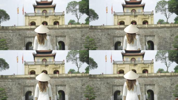 越南女子穿着传统服饰，戴着亚洲风格的圆锥形帽子，走在唐龙御城
