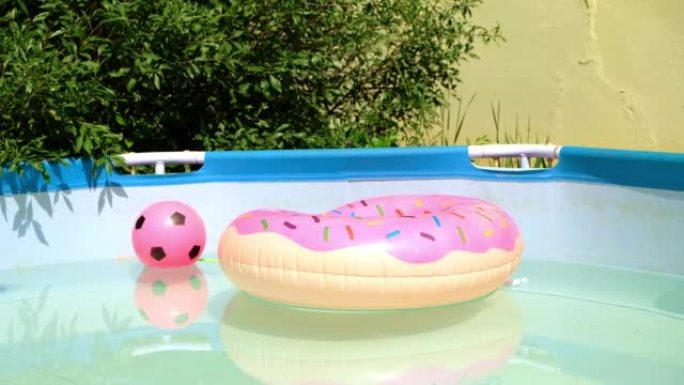 在阳光明媚的夏日，儿童游泳池，粉红色的球和甜甜圈漂浮。花园游泳池里的充气泳池玩具甜甜圈。