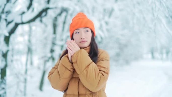 年轻的亚洲女孩冻结在公园里等待约会，在冬天下雪的日子里，一个女人穿着暖和。在雪的背景下，户外女性冰冻