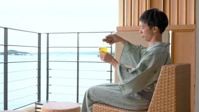 亚洲男子在温泉客栈边看海边喝啤酒