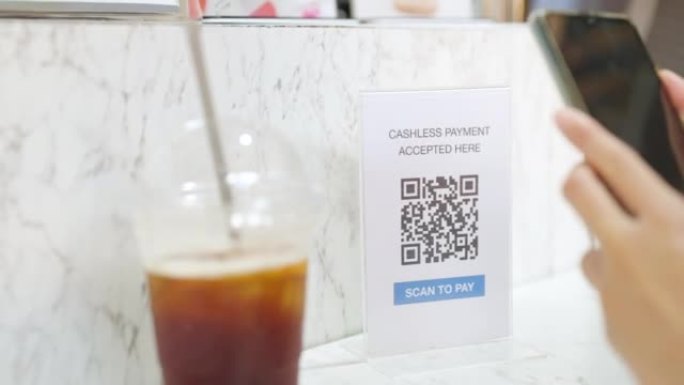 4k年轻的亚洲女性使用手机扫描二维码进行在线支付在咖啡店购买冰咖啡。