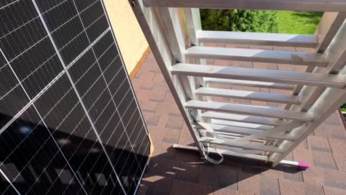 光伏太阳能电池板靠在墙上，准备安装在沥青瓦屋顶上。金属梯子准备安装