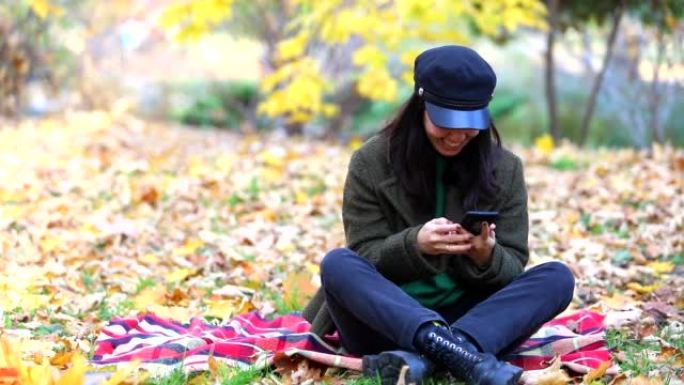 秋天公园的毯子上坐着电话的幸福女人