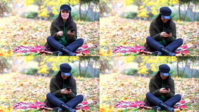 秋天公园的毯子上坐着电话的幸福女人