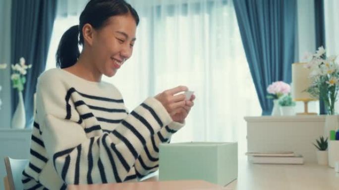 兴奋的年轻亚洲女孩穿毛衣收到礼物打开开箱薄荷粉色粉盒玻璃商店礼物，桌子上有快乐的时刻。