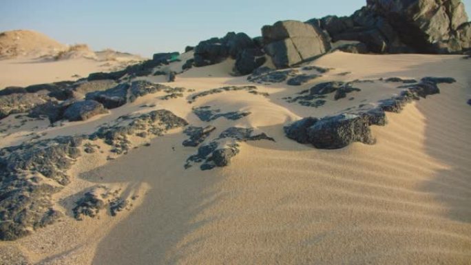 海滩上白色细沙的特写镜头。金色的沙子运动，海边有纹理的黑色火山石。沙漠沙丘的美丽