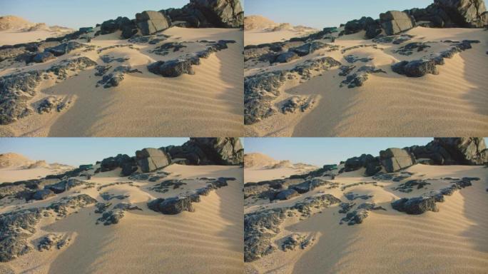 海滩上白色细沙的特写镜头。金色的沙子运动，海边有纹理的黑色火山石。沙漠沙丘的美丽