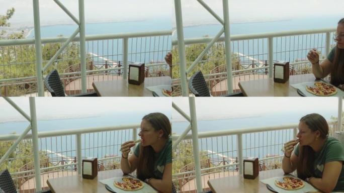 一个女孩坐在山顶的咖啡馆里。这里有美丽的海景。她吃披萨。夏。在运动中。