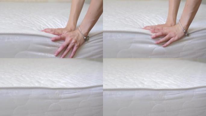 一个女孩的手的特写检查一个新的舒适的矫形白色床垫的刚度。女性手压在矫形表面。女孩测试弹性柔软矫形床垫