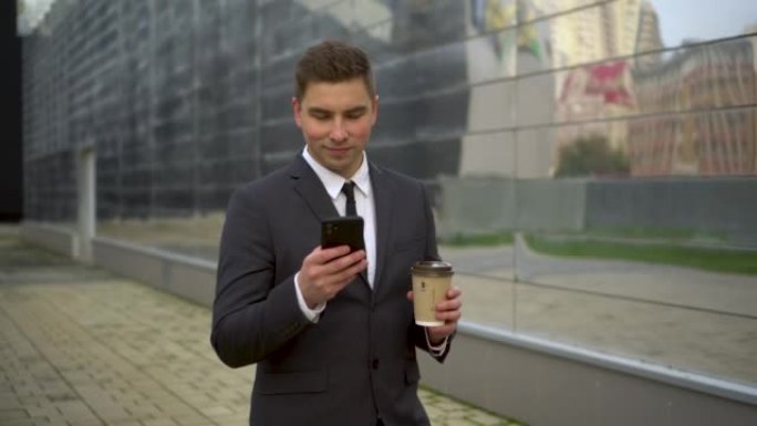 一个年轻的商人正在打电话发短信，喝咖啡。一个穿着西装的英俊男子手里拿着智能手机喝咖啡。4k