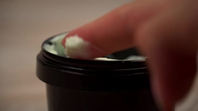 一罐奶油躺在桌子上，一个女人的手指捡起它