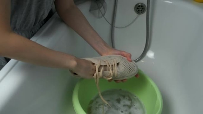 女人正在用手用海绵，特写手在盆子里洗运动鞋。