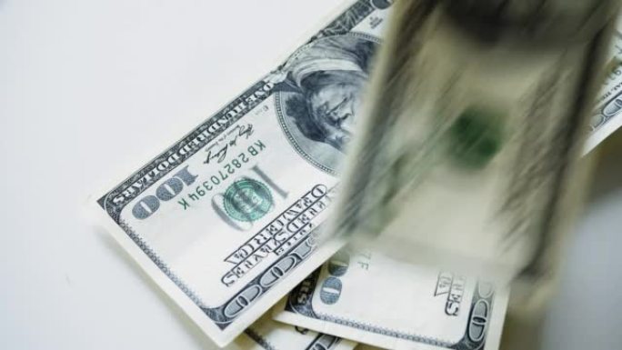 从俯视图看，一张不同面额的美国钞票落在一张白色的桌子上。数钱——俯视图。慢动作视频。