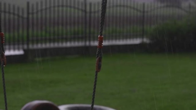 在雨中，水从握住秋千的绳子上滴落。