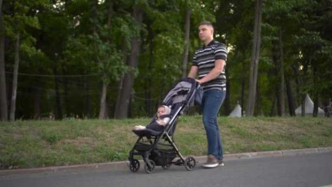 一个年轻人正带着婴儿车穿过公园。父亲和儿子在大自然中行走。