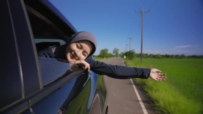 自由微笑的穆斯林妇女在穿过乡间小路时将手臂伸出车窗。