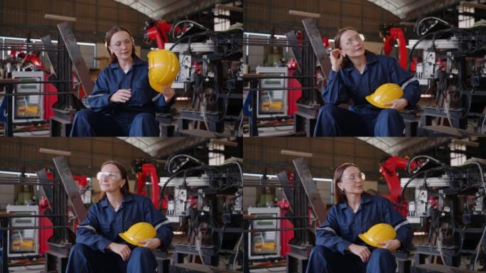 工业年轻女工穿着安全帽安全服站在工程师仓库里，背景是机器人手臂微笑着看着相机
