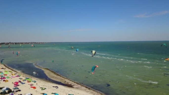 许多风筝冲浪者的天线，五颜六色的风筝飞过蓝色的泻湖，骑在风筝板上。在大风天，风筝冲浪者用降落伞在海浪