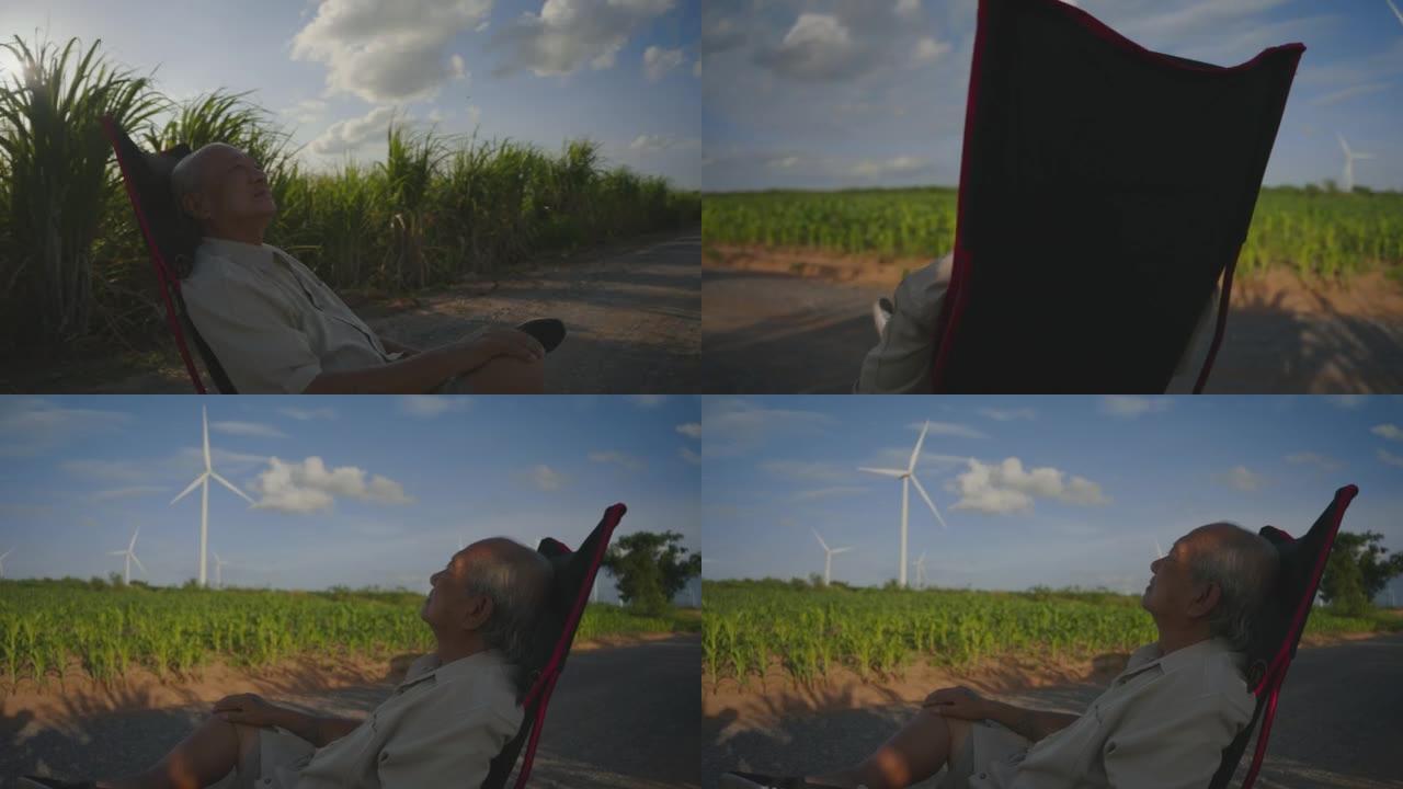 快乐的高级男人晚上坐在风力涡轮机农场的椅子上