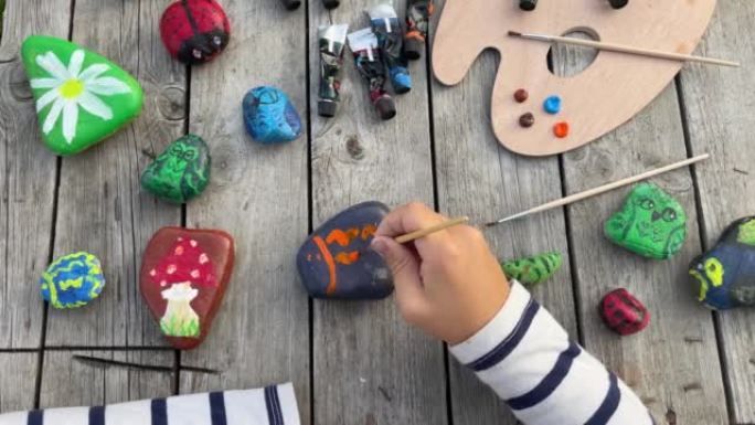 一个孩子的手用丙烯酸颜料在石头上画真菌的镜头。家庭爱好是真实的。