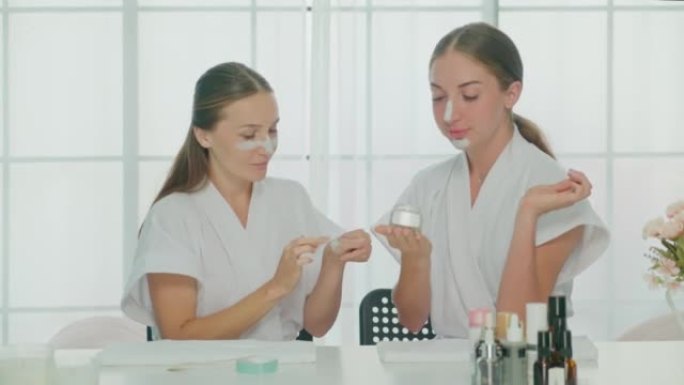 Two beautiful women in bathrobes applying moisturi