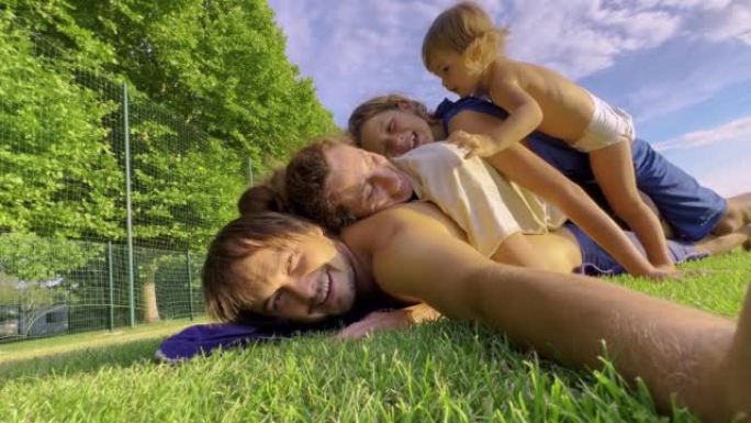 一个幸福的四口之家正在绿草地上玩耍。可爱的孩子爬到父母的身上嬉笑嬉戏。公园里友好的家庭