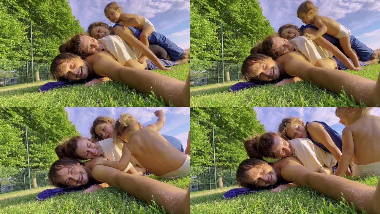 一个幸福的四口之家正在绿草地上玩耍。可爱的孩子爬到父母的身上嬉笑嬉戏。公园里友好的家庭