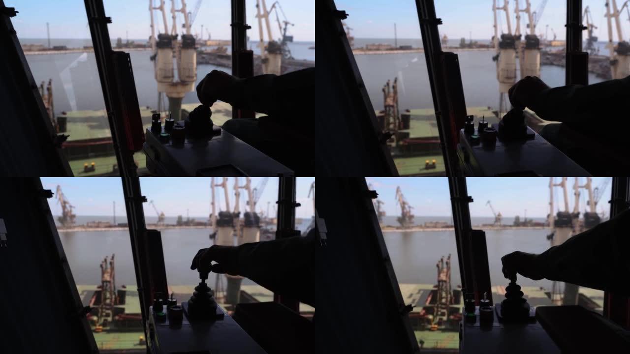 男子双手控制谷物码头操作员舱工作场所的操纵杆。工人通过在码头上移动行李箱机，用臂杆手柄控制从筒仓到散