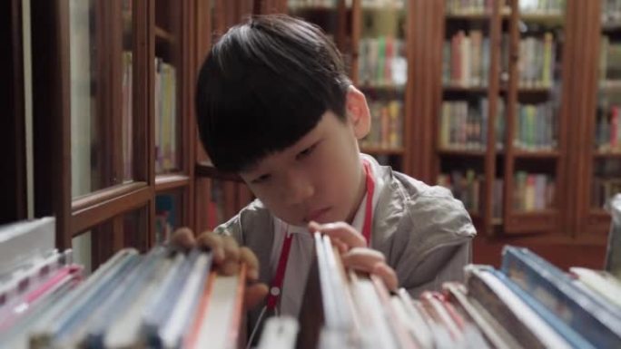 可爱聪明的亚洲小学生男孩在图书馆的木制书架上寻找书