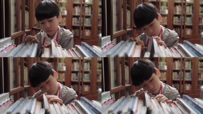 可爱聪明的亚洲小学生男孩在图书馆的木制书架上寻找书