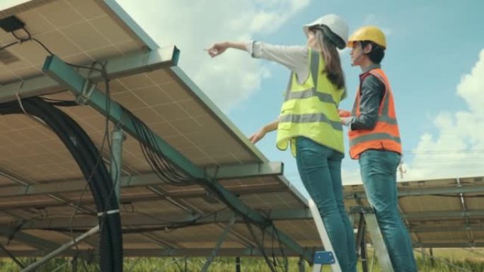 两名穿着制服和安全帽的工人在太阳能农场中检查太阳的运行和光伏太阳能电池板的清洁度。生态概念