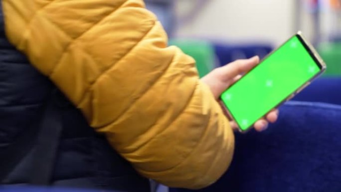 绿屏和火车在线浏览的man watch智能手机的背面视图。模拟观看手机上的内容。站在公共交通工具室内