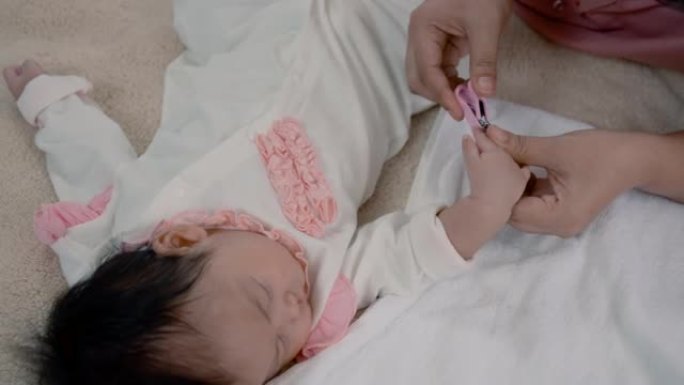4K，一个女婴睡在棕色的床上，舒服，妈妈抽出宝宝睡觉的时间，带上剪刀给熟睡的宝宝剪指甲，小心翼翼，让