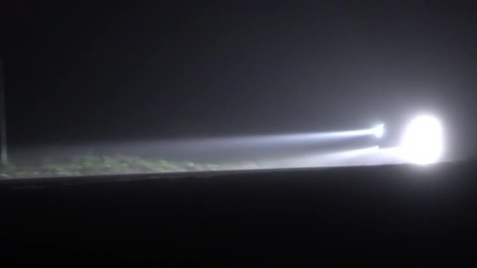 大雾中的汽车在空旷的夜晚乡间小路上行驶。在完全黑暗的环境中，只能看到汽车前灯的明亮光线。