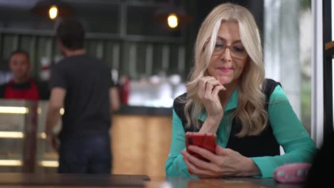 高级女行政女性在咖啡店使用智能手机。犹豫不决的老年人在线浏览互联网坐在咖啡馆餐厅
